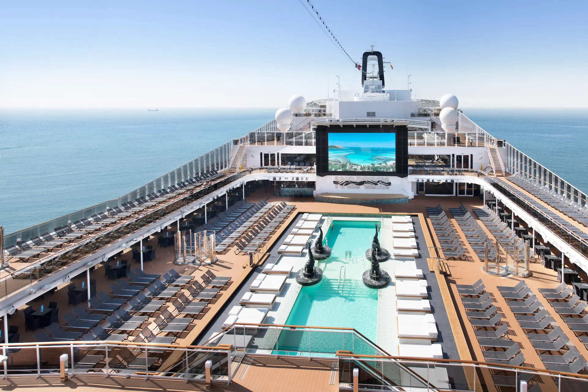 Zwembaddek van MSC Bellissima met ligbedden en groot buitenscherm.