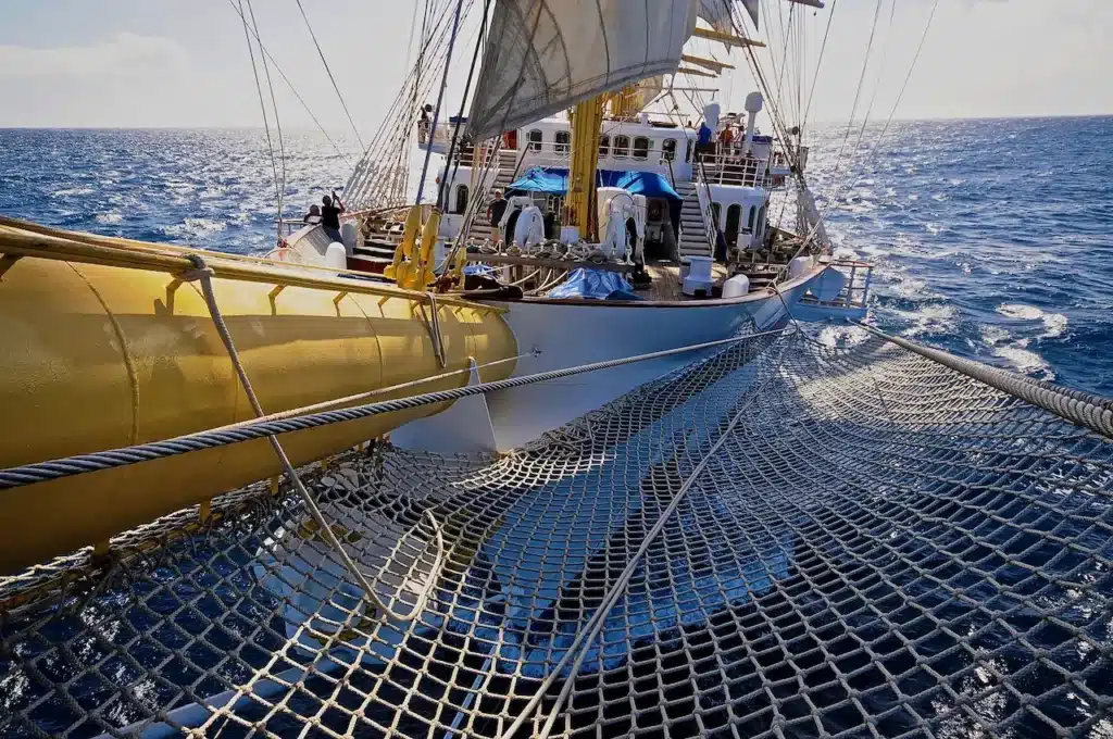 Zicht vanaf de boegspriet van een Star Clippers zeilschip over het net naar het voordek, varend over een glinsterende blauwe zee.