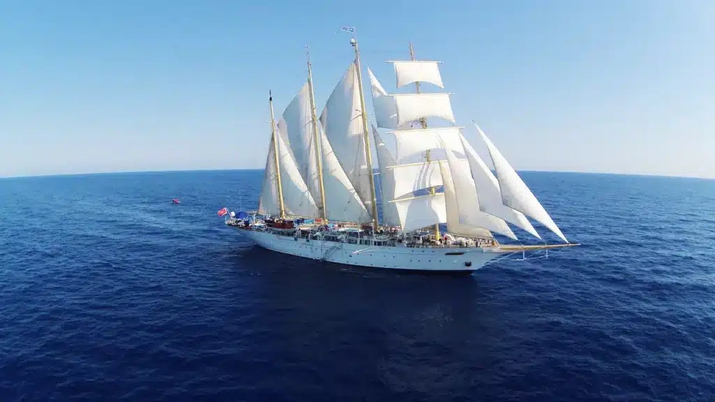 Een indrukwekkend zijaanzicht van de Star Clipper of Star Flyer, varend op een diepblauwe oceaan met alle witte zeilen volledig gehesen onder een strakblauwe lucht.