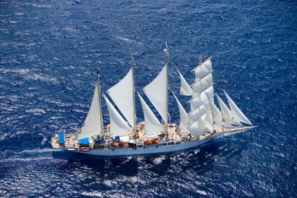 Een indrukwekkend bovenaanzicht van de Star Flyer of Star Clipper, een viermast-zeilschip dat met volle zeilen door de diepblauwe oceaan vaart.