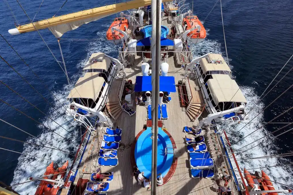 Het sfeervol verlichte houten buitendek van de Royal Clipper 's nachts, met zicht op de Tropical Bar en de indrukwekkende masten die oprijzen tegen de donkere hemel.