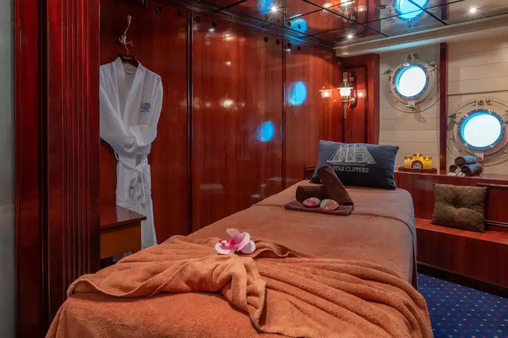 Een sfeervolle massagekamer in de Captain Nemo Spa aan boord van de Royal Clipper, met een massagetafel, luxe handdoeken, houten wanden en unieke patrijspoorten onder de waterlijn.