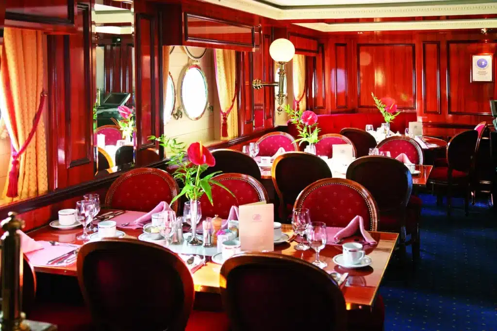 Het elegante restaurant 'Clipper Dining Room' aan boord van de Royal Clipper, met gedekte tafels, rood fluwelen stoelen, rijke houten lambrisering en klassieke patrijspoorten.