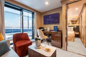 De luxe Journey Suite op een Atlas Ocean Voyages schip met een zithoek, zicht op de slaapkamer en balkon met zeezicht.