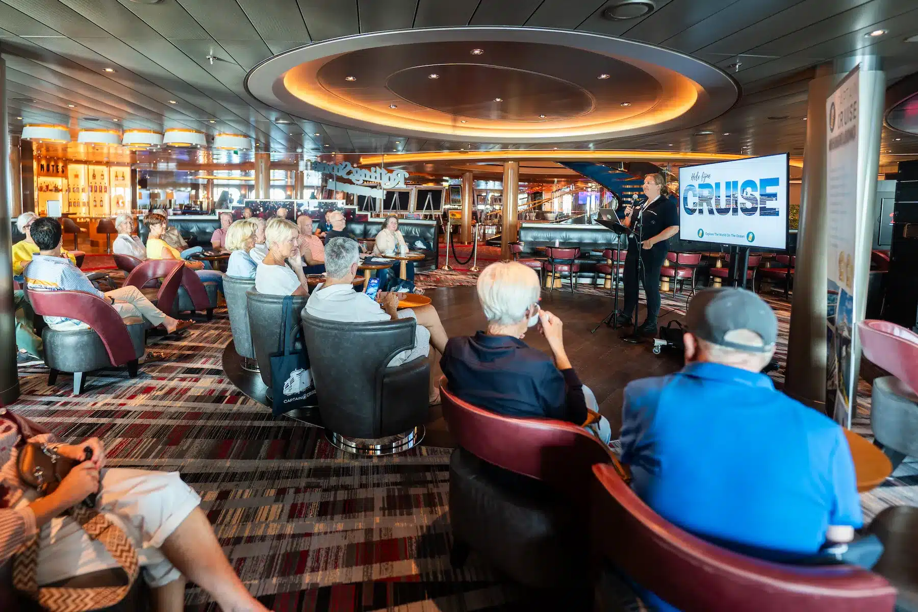 Welkomstpresentatie tijdens het hospitality uur waarbij de Captain Cruise reisbegeleider passagiers informeert in de lounge aan boord van het cruiseschip