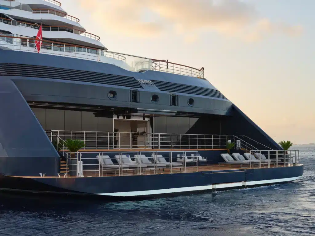 Achterdek van een luxe jacht van The Ritz-Carlton Yacht Collection met loungebedden en uitzicht op zee tijdens zonsondergang.