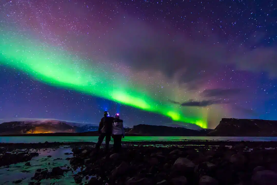 Noorderlicht boven een IJslands landschap met twee mensen die de aurora borealis bekijken