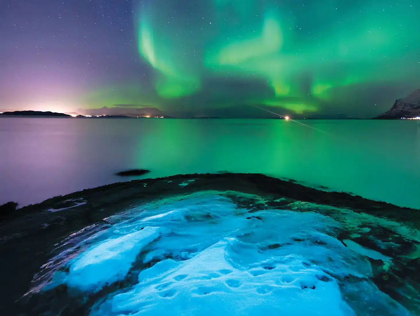 Noorderlicht boven een bevroren Noors winterlandschap met weerspiegeling in het water.