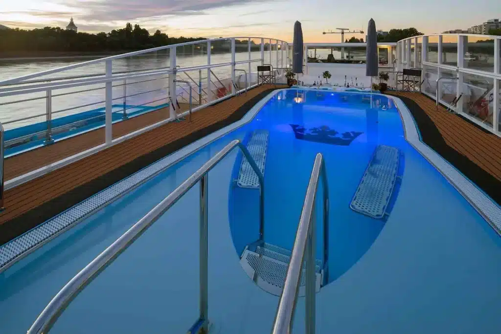 Het zonnedek van de AmaFiora met een zwembad voorzien van het AmaWaterways-kroonlogo, een bar met drankflessen en parasols.