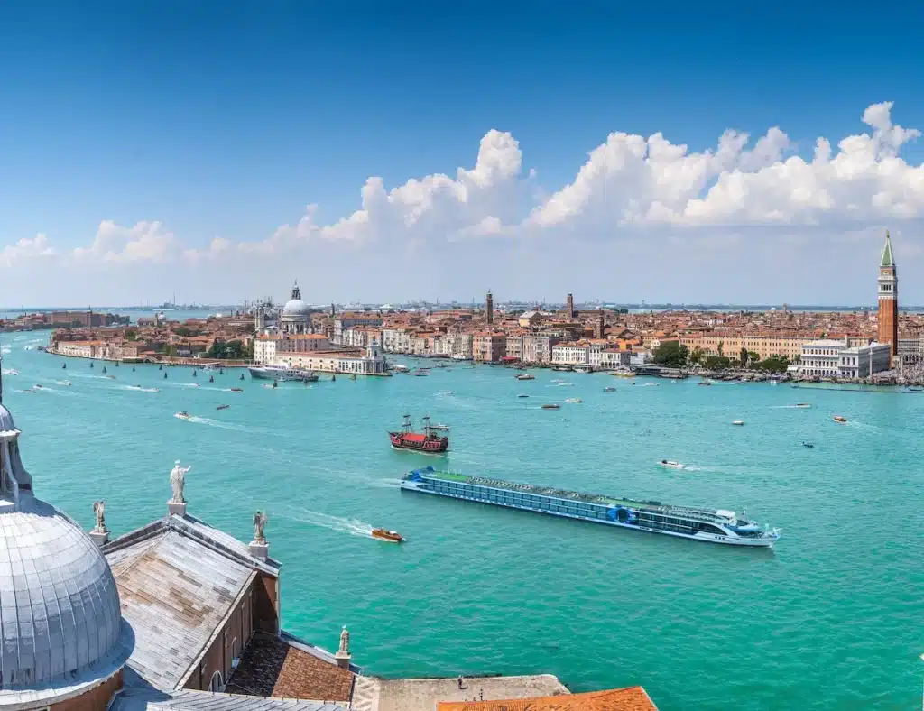 Luchtfoto van het VIVA Cruises riviercruiseschip VIVA Unique varende door de lagune van Venetië, met uitzicht op het San Marcoplein en de historische skyline.