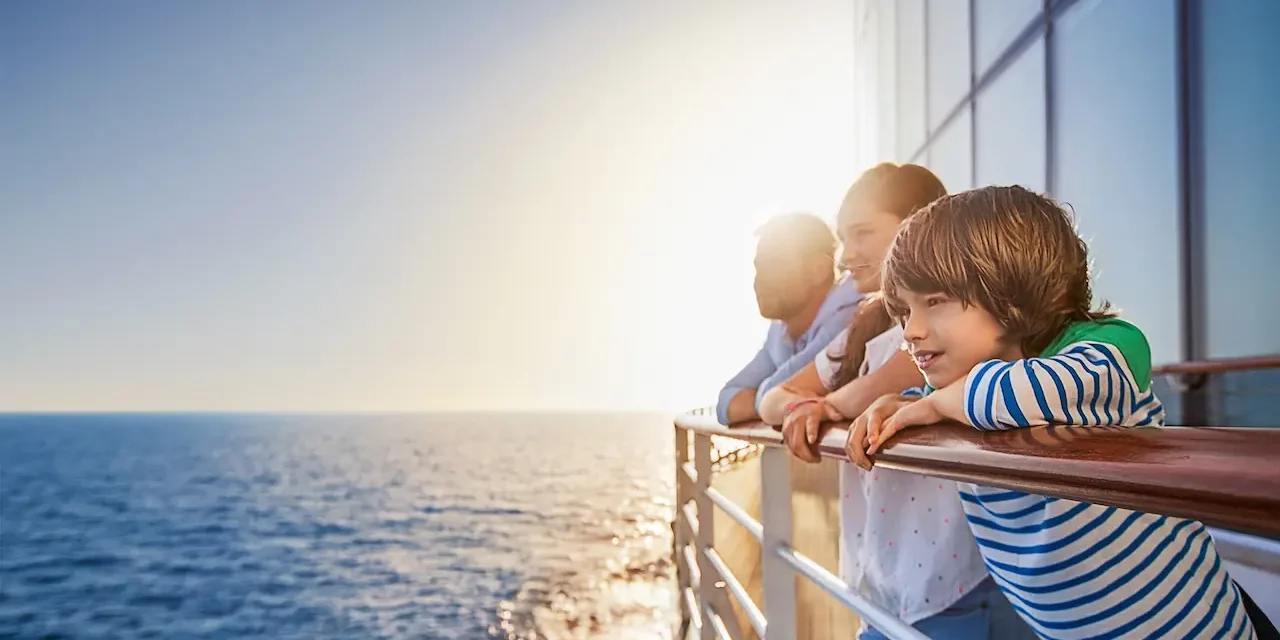 Een vader met twee kinderen die vanaf de reling van de AIDAperla of AIDAprima over de zonnige oceaan uitkijken tijdens hun cruisevakantie.